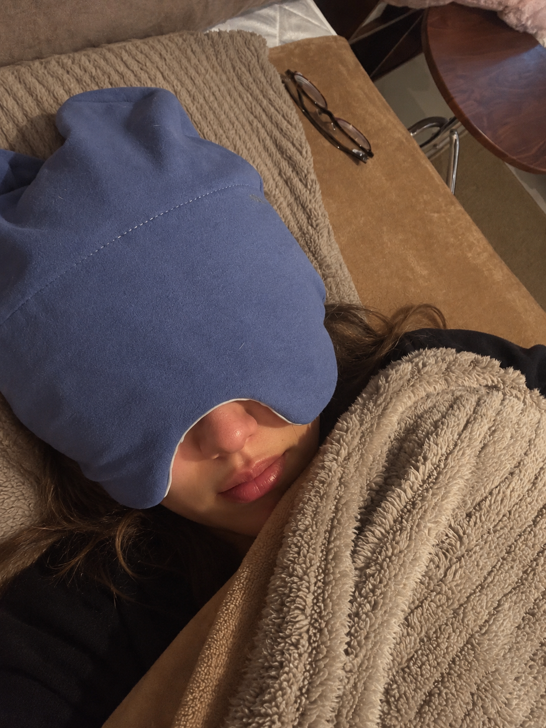 Person resting under a blanket wearing the blue weighted sleep hood