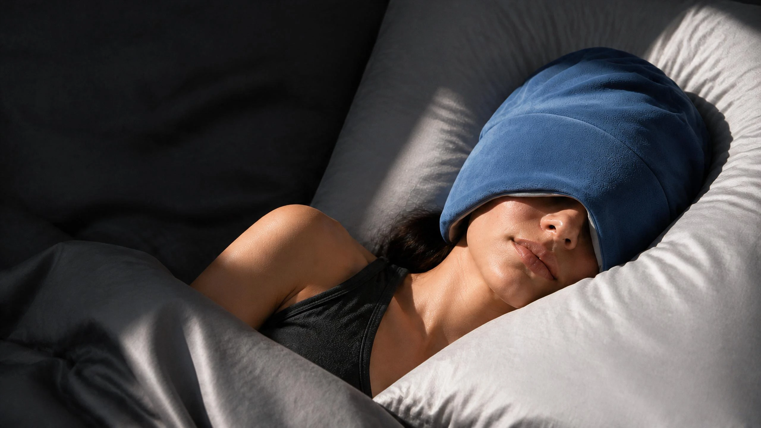 Woman resting on a grey pillow wearing the blue MYSLUNA weighted sleep mask