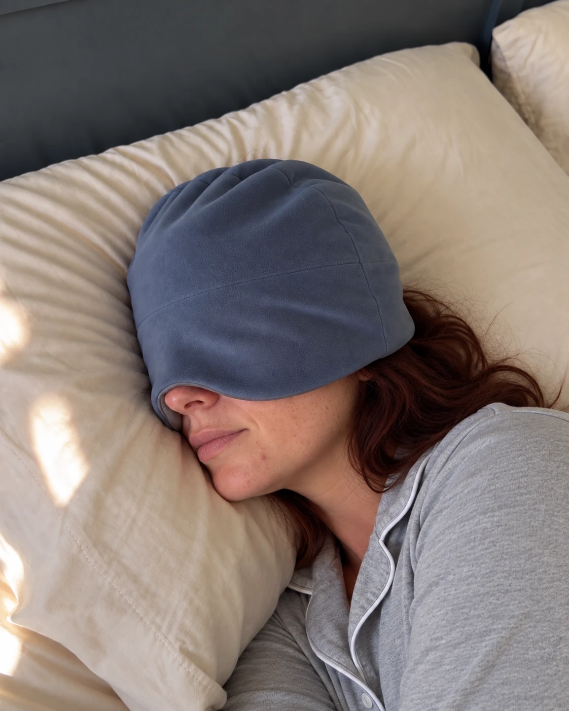 Woman resting on her side wearing the blue weighted sleep mask on a cream pillow